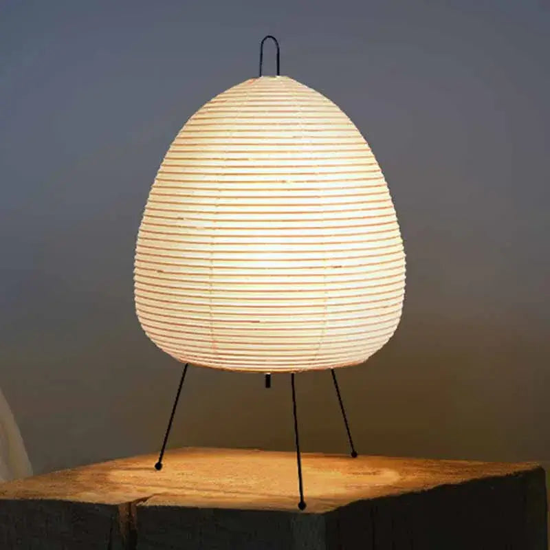 Warmly glowing akari noguchi table lamp with egg-shaped rice paper shade and black metal tripod base for home decor