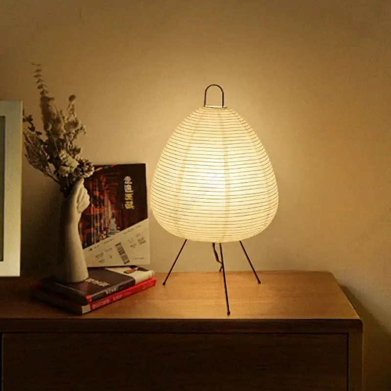 Warmly glowing akari noguchi table lamp with ribbed off-white rice paper shade and black metal tripod base for home décor