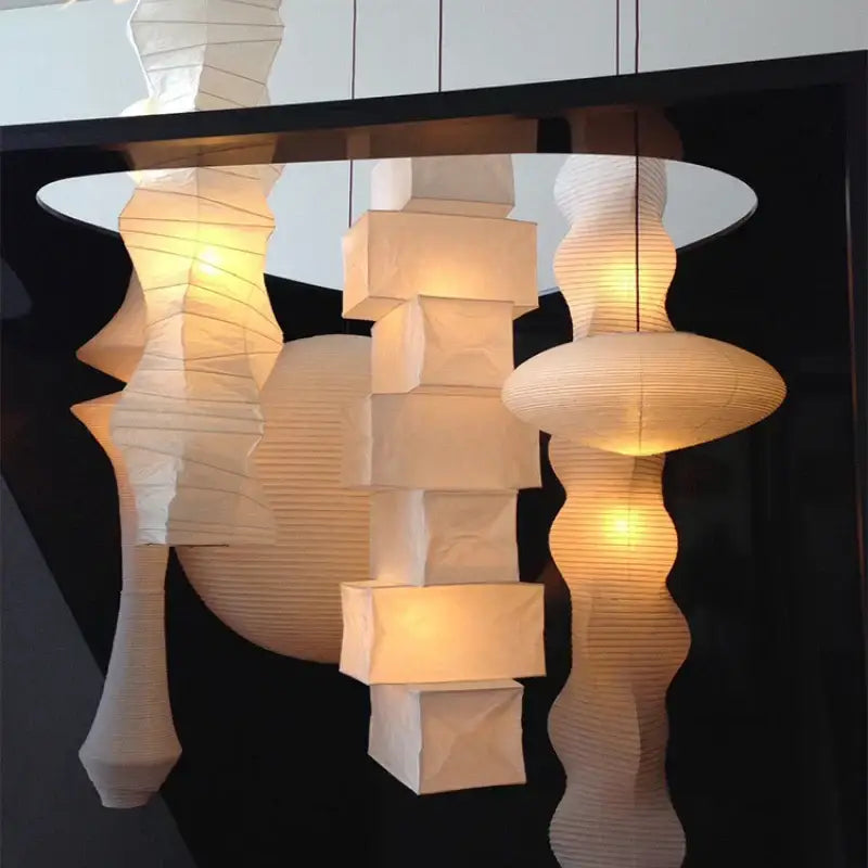 A collection of illuminated white akari rice paper pendant lamps with geometric and organic shapes for living spaces