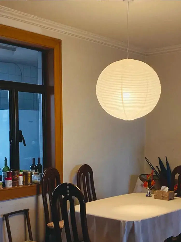 A spherical off-white akari rice paper pendant light hanging by a thin cord for home décor illumination