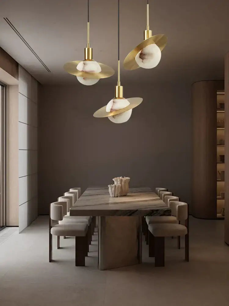 Three elegant gold-toned alabaster marble pendant lights with frosted glass shades hang above a modern dining table