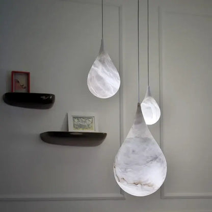 Three alabaster marble pendant lights with white marble finish and gray veining for luxury dining room décor