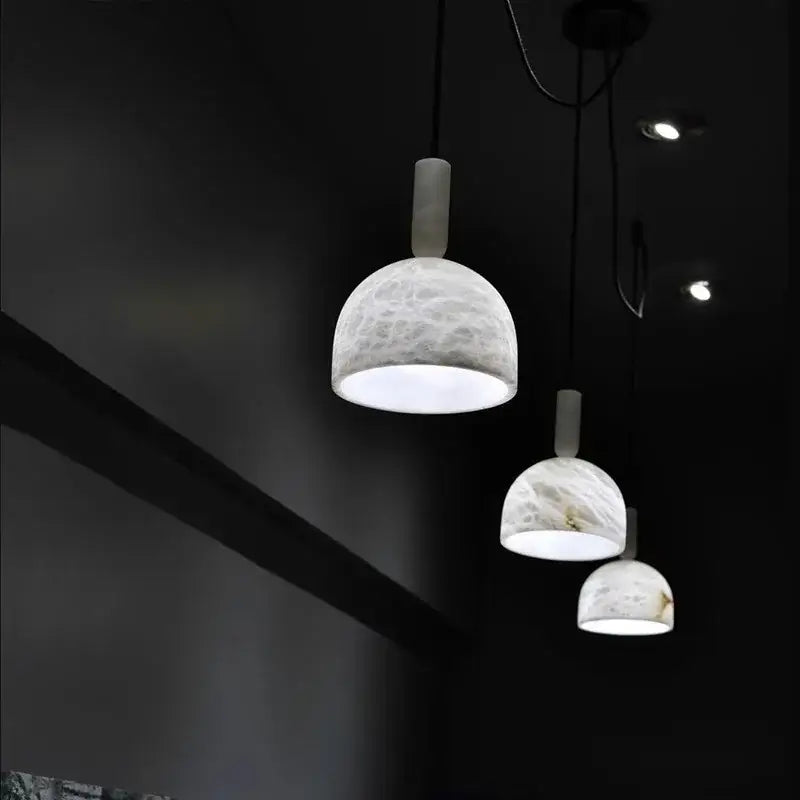 Three elegant white marble alabaster pendant lights with cylindrical necks hang in a modern living room setting