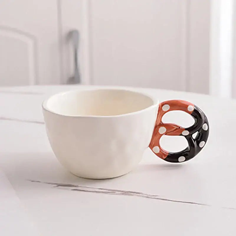 White ceramic alkali water biscuit mug with playful pretzel-shaped handle in black orange and white polka dots