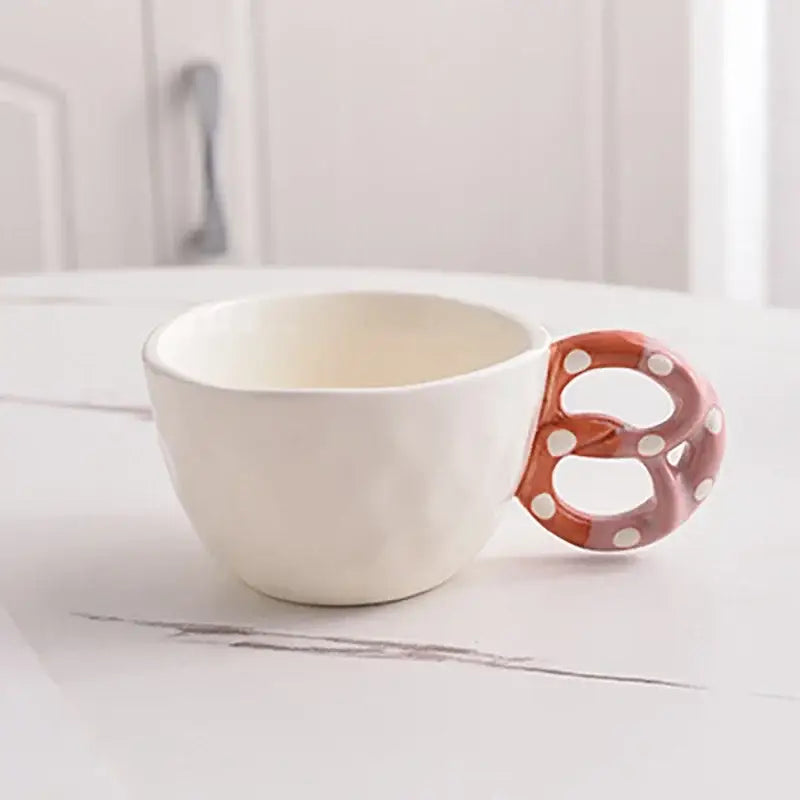 Decorbites alkali water biscuit ceramic mug set featuring a white mug with an orange pretzel-shaped handle and polka dots