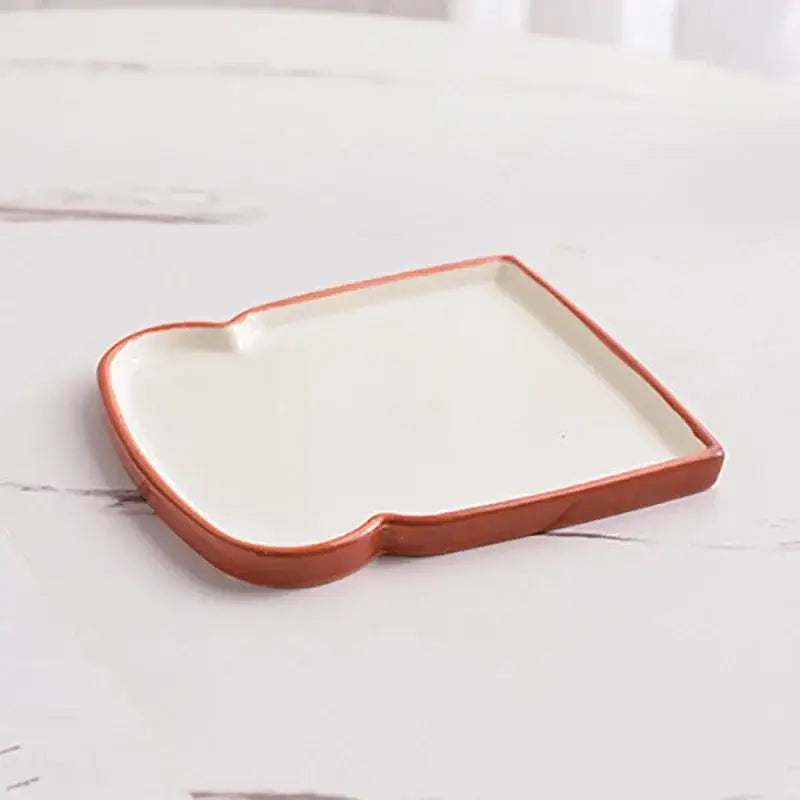 A ceramic toast-shaped tray with a white interior and terracotta rim for the decorbites alkali water biscuit mug set