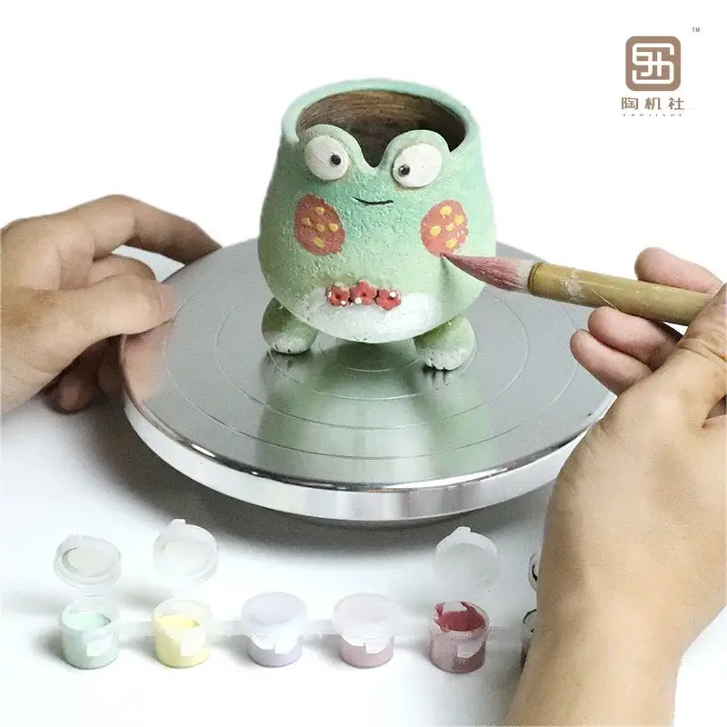 A green frog-shaped ceramic planter with orange spots displayed on a silver aluminum alloy turntable for clay sculpture