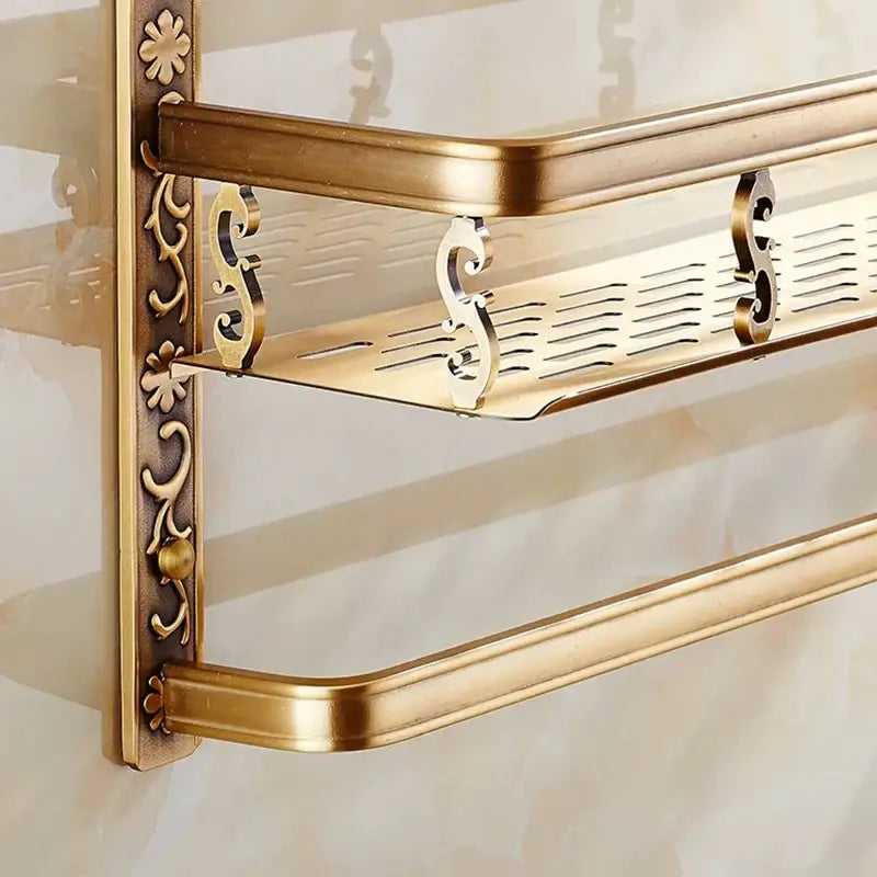 Gold-toned aluminum bathroom corner shelf with ornate floral detailing, solid top shelf, and ventilated perforated lower shelf