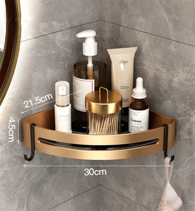 Gold-colored aluminum bathroom corner shelf with black hooks and central cutout holding various bathroom products