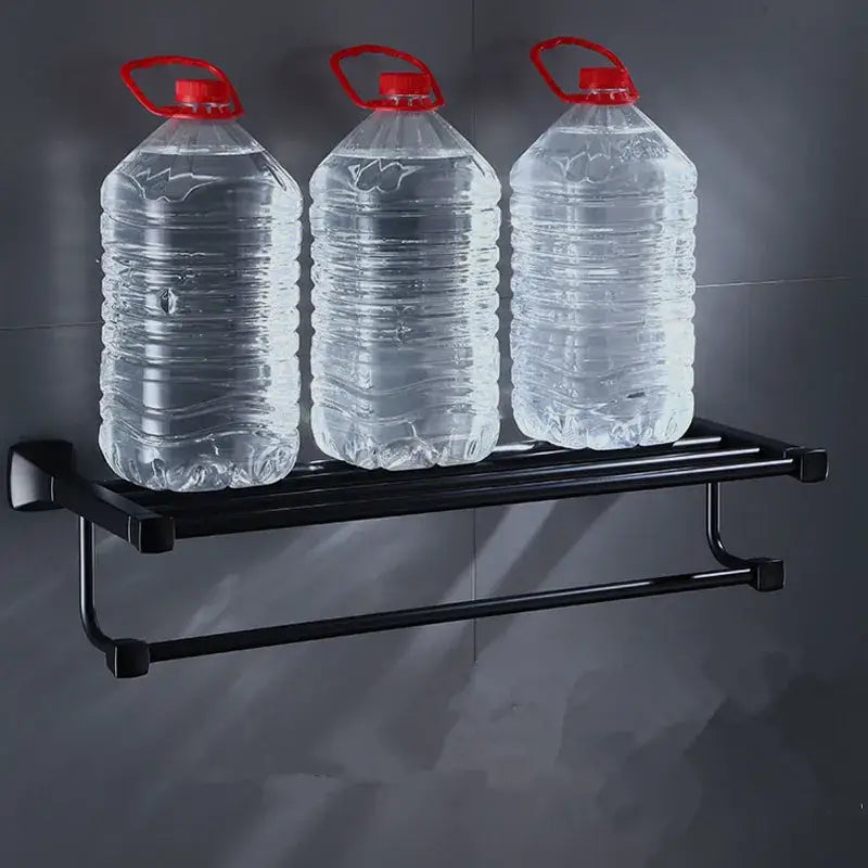 Black aluminum metal wall-mounted corner shelf holding three clear water jugs with red caps in bathroom hardware set