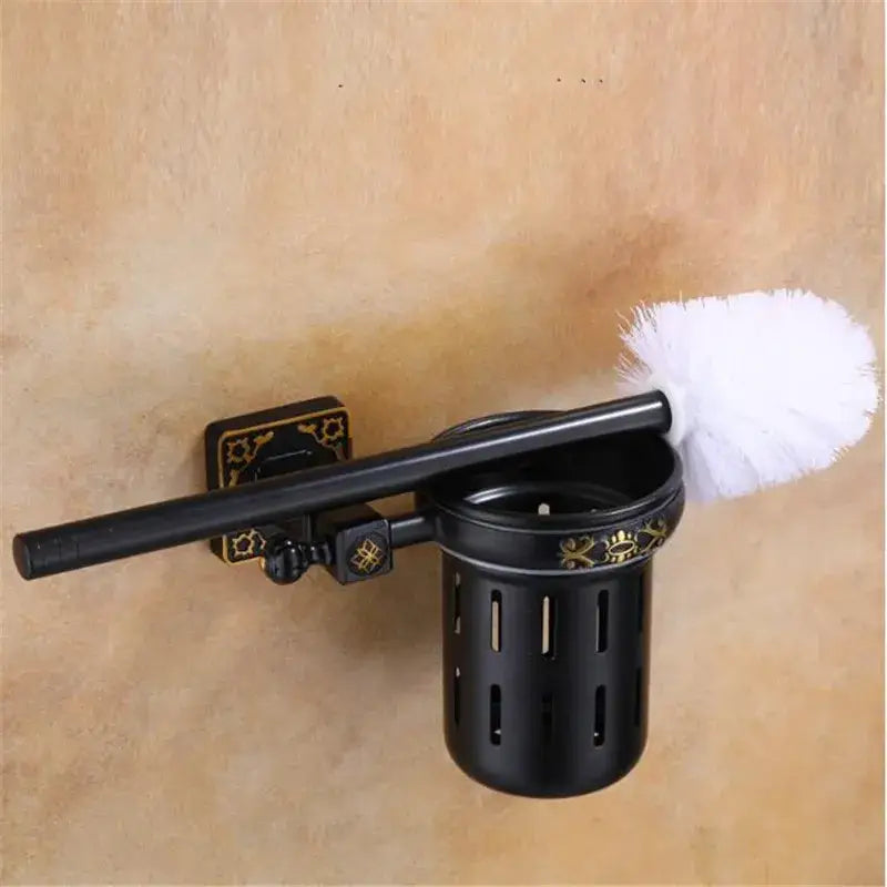 Decorbites aluminum carved black metal toilet brush holder with gold floral accents holding white bristle brush