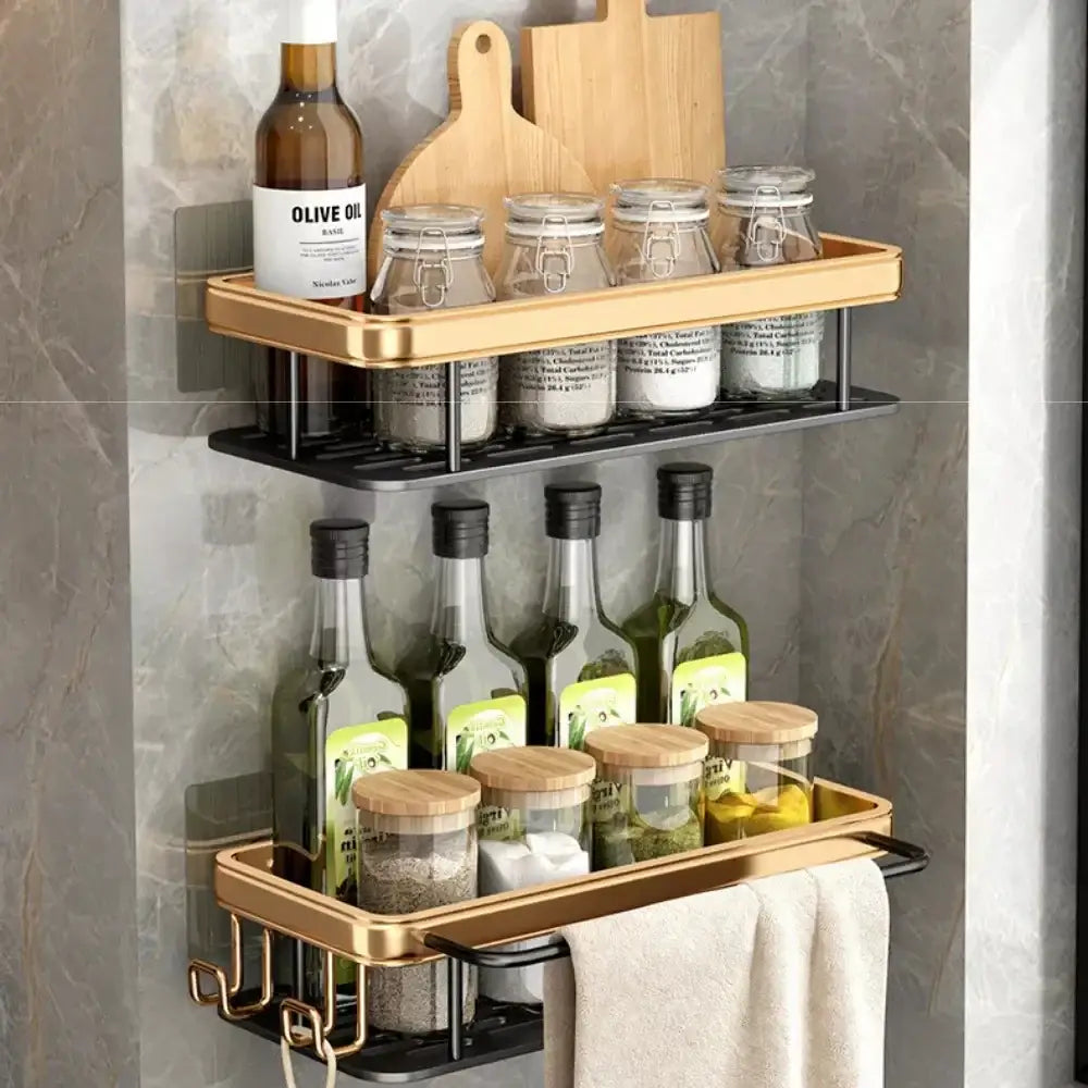 Two-tiered aluminum corner bathroom shelf with towel holder featuring gold and black metal shelves holding jars and bottles