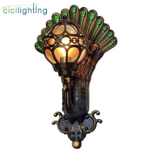 Peacock-themed wall lamp with ornate black metal frame, green blue stained glass feathers, and amber aluminum globe glass shade