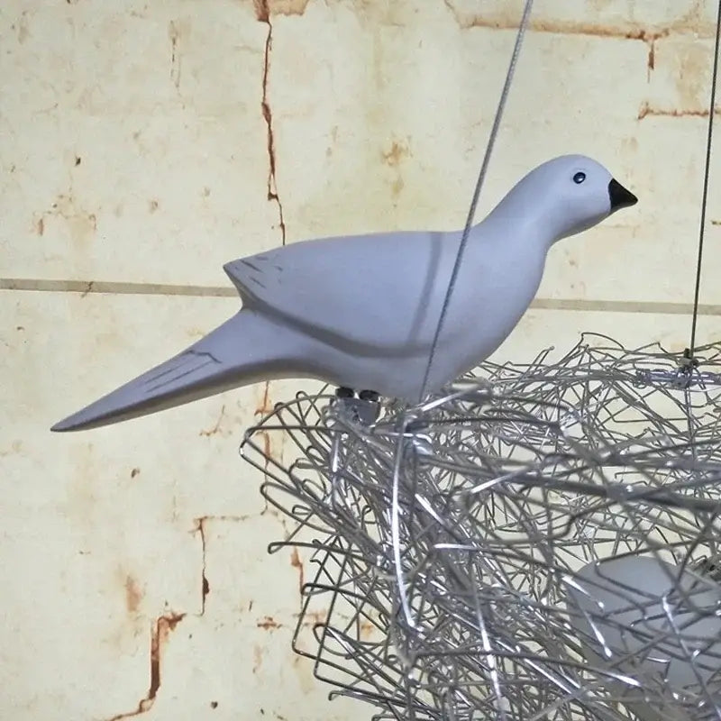 A sleek matte gray ceramic dove with black beak perched on intricate aluminum wire bird’s nest pendant lights
