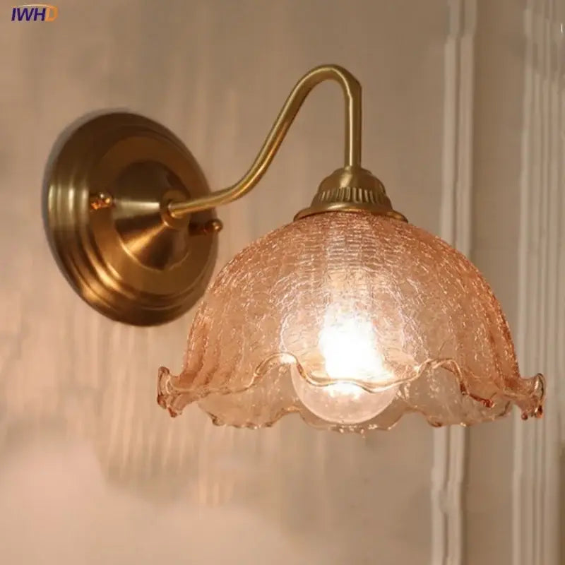 Antique brass wall sconce with amber flower glass featuring a textured peach shade and ruffled edges for living room use