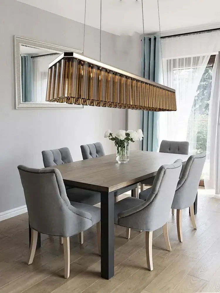 A modern amber glass ceiling chandelier with gold-toned vertical slats hanging above a dining table