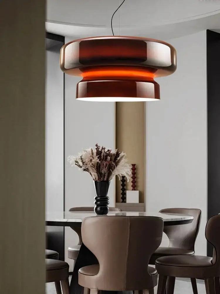 A modern tiered pendant light with amber glass ceiling and metallic accents hanging above a dining table