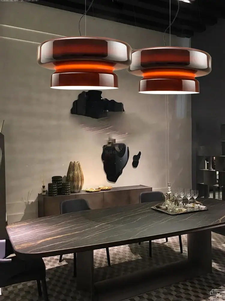 Two sleek tiered pendant lights with amber glass ceiling and metallic finish hang above dining table by decorbites