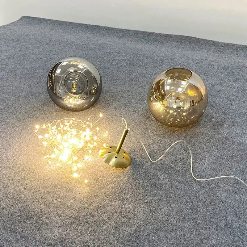 Two spherical glass lamps with amber glass and mirrored silver finishes rest on gray surface with golden base for luxury lighting