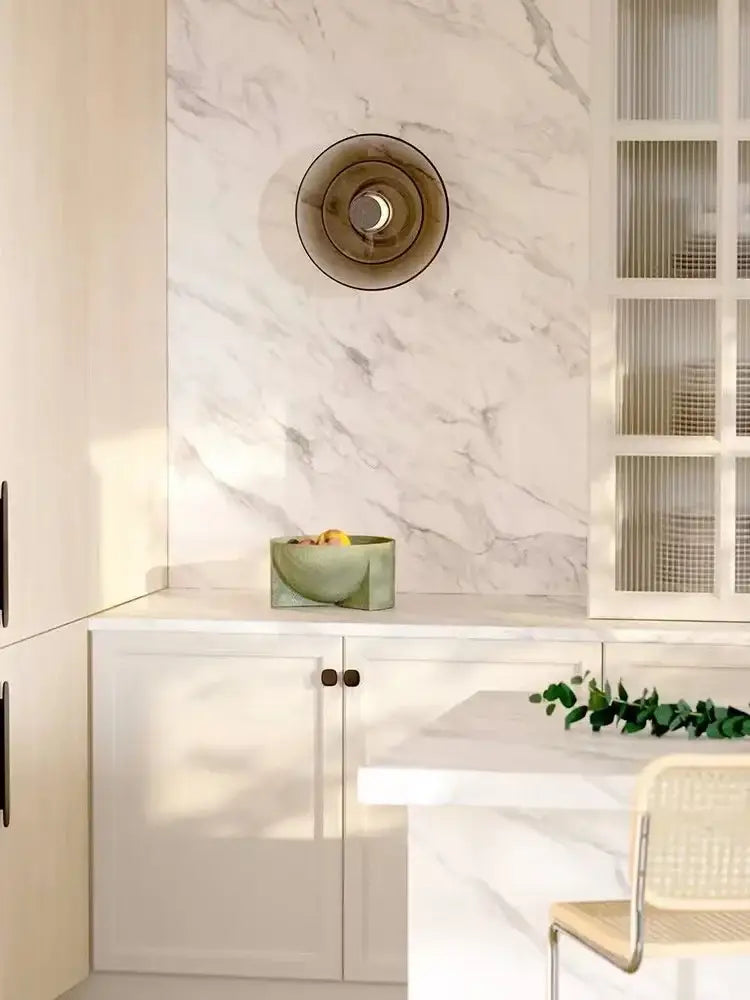 A sleek matte sage green ceramic bowl with a modern geometric design beside DecorBites amber glass disc wall lamp