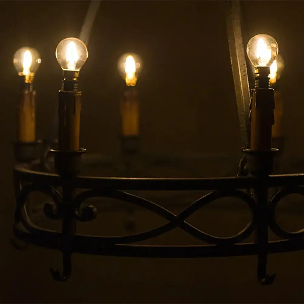 Dark wrought iron chandelier with multiple glowing amber glass led filament bulbs suitable for dimmable outdoor use