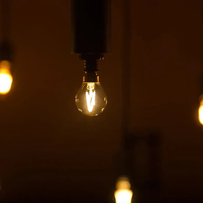 Warmly glowing DecorBites™ amber glass led filament globe bulb with clear glass and visible filament in dark metal fixture
