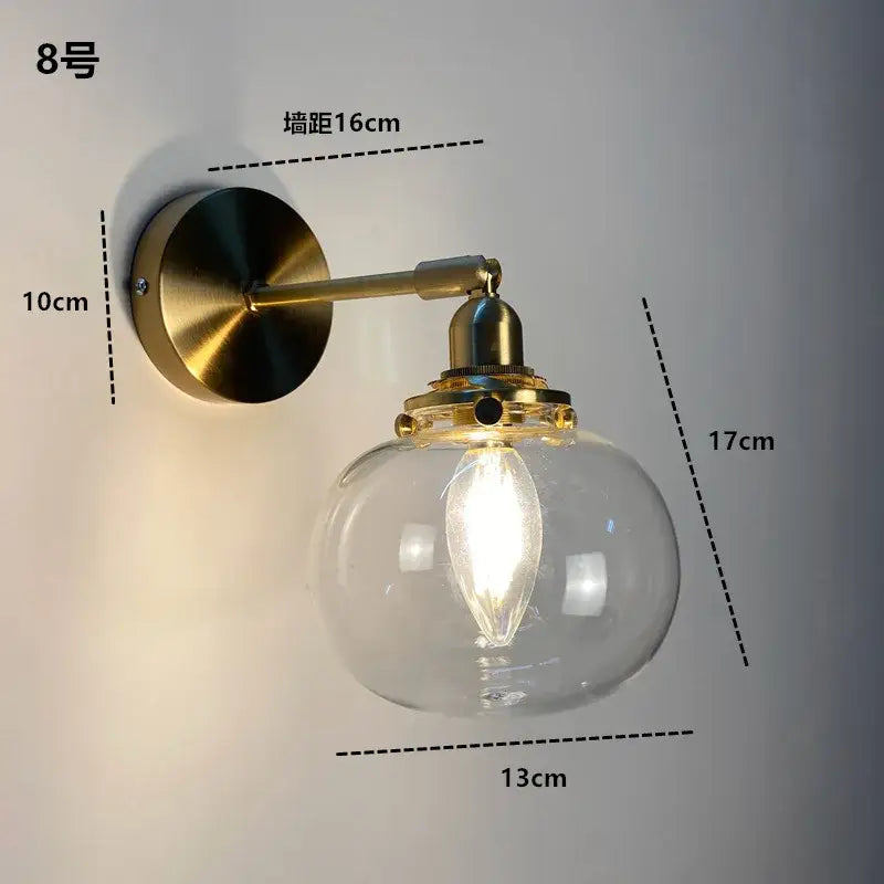 Brass-finished wall light fixture with a clear glass globe and exposed filament bulb for modern lighting use