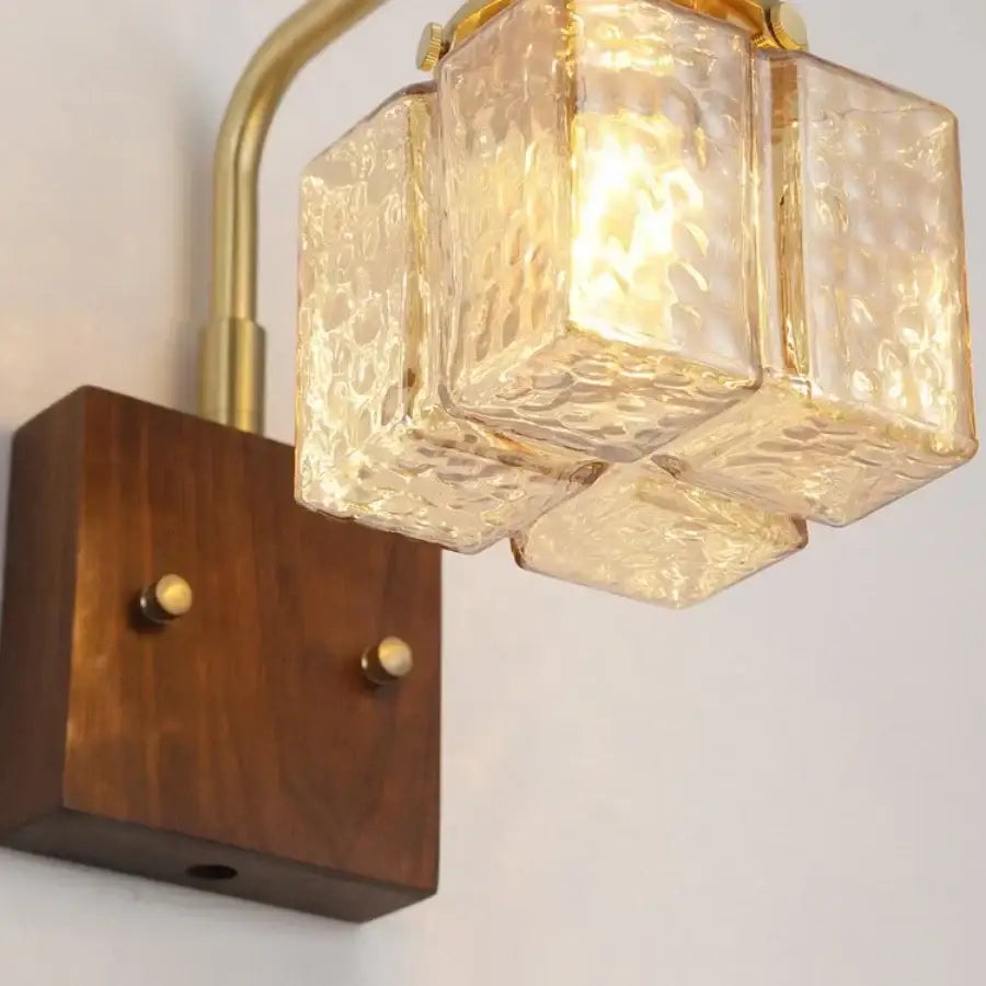DecorBites amber glass LED wall sconce with walnut wood base and brass arm emitting a warm golden glow
