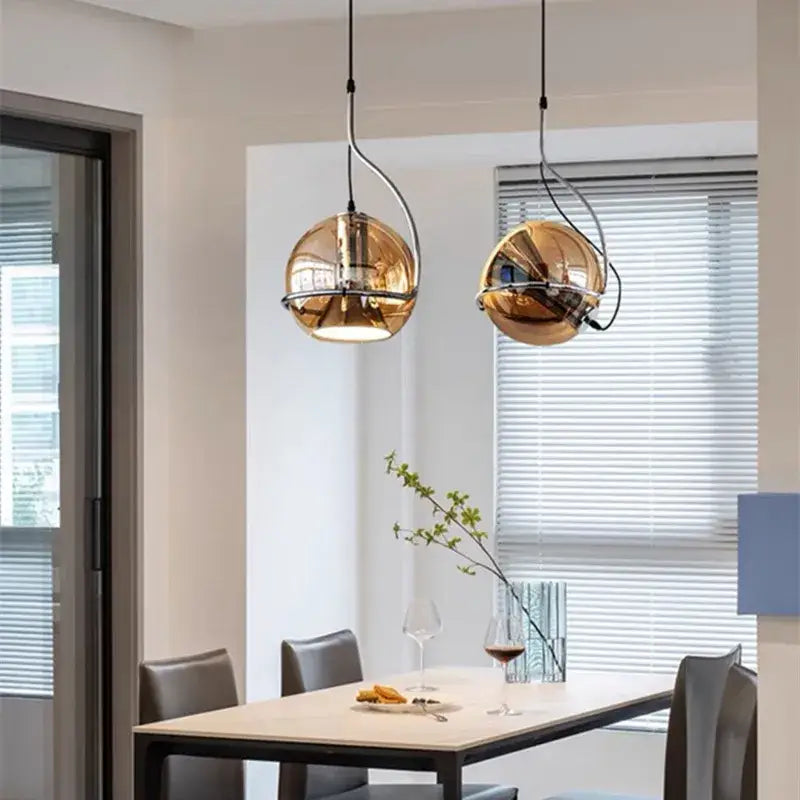 Two spherical gold decorbites amber glass pendant lights with reflective finish hanging above a dining table