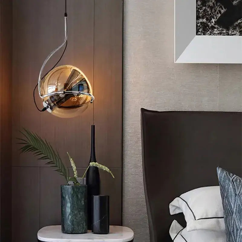Golden spherical decorbites amber glass pendant light with sleek chrome wire frame hanging above marble nightstand