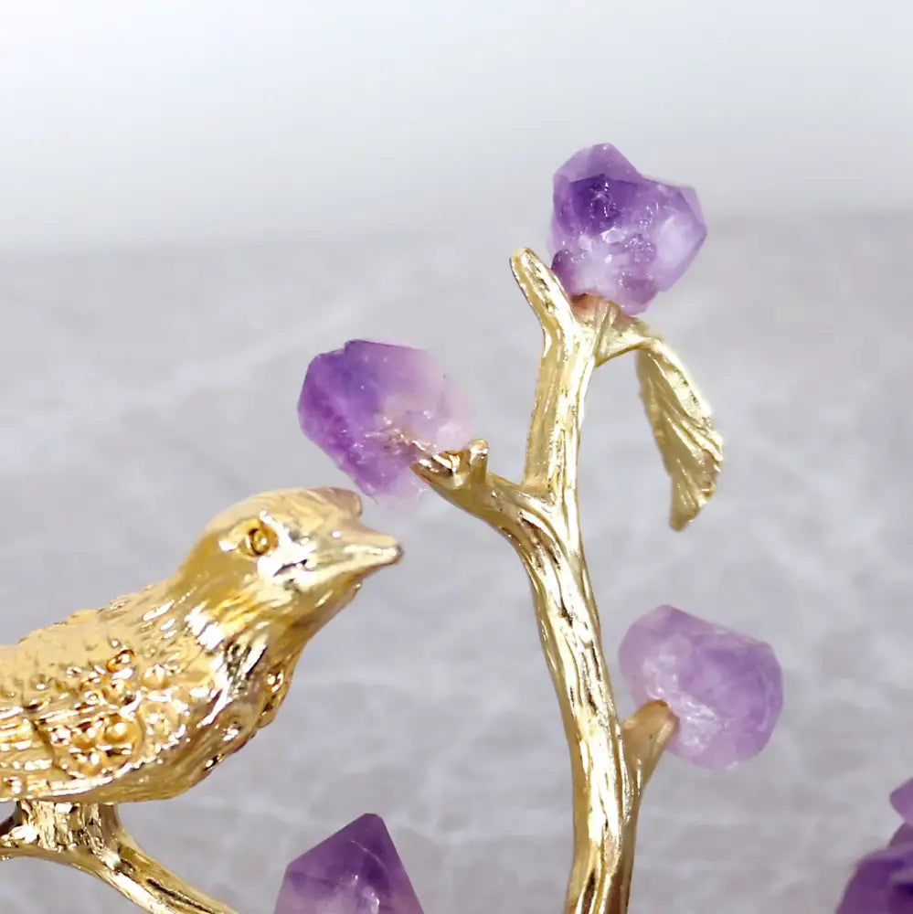 Golden bird figurine perched on a branch with raw purple amethyst crystals amethyst flower ball bird sculpture