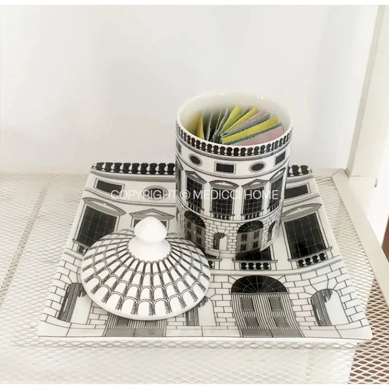 White ceramic tea canister with black ancient roman architecture design and ornate lid filled with colorful tea bags