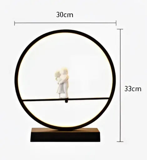 Black circular frame table lamp with minimalist design featuring two white angel doll bird figurines on a horizontal bar