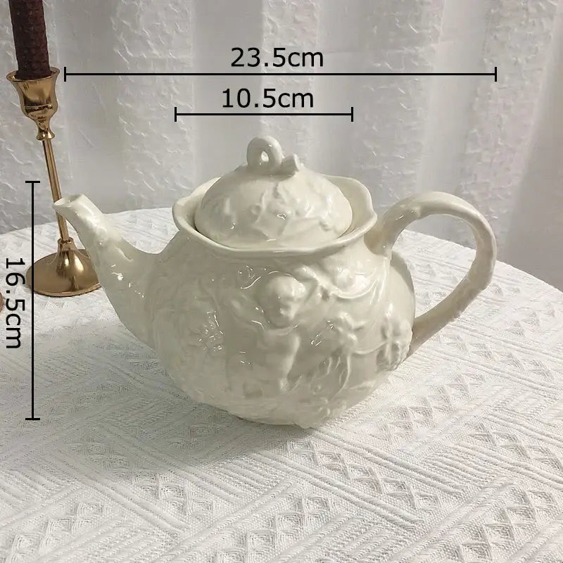 A white ceramic teapot with intricate angel figures relief and matching lid from DecorBites™ dining set and mug collection
