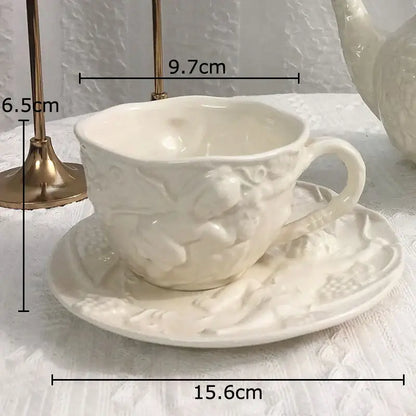 White porcelain teacup and saucer with intricate embossed floral and angel figures relief detailing by DecorBites™