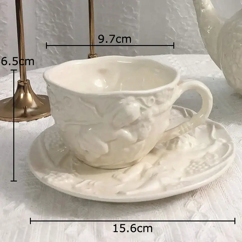 White porcelain teacup and saucer with intricate embossed floral and angel figures relief detailing by DecorBites™