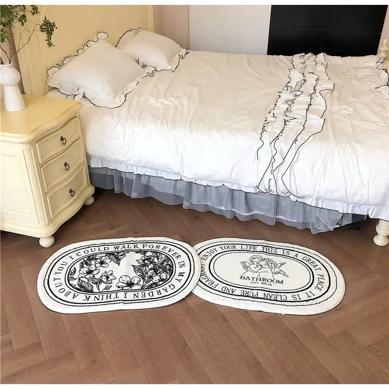Two oval-shaped white bath rugs with black floral angel print shaggy design and ruffled edges 40x60cm decorbites