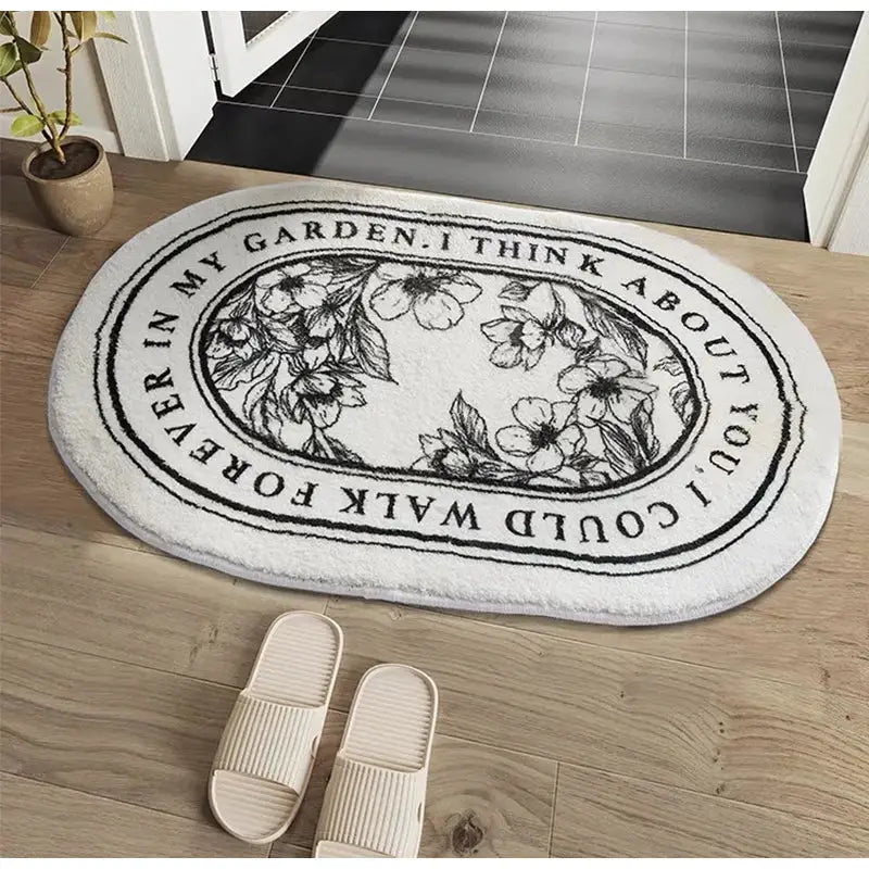 White oval-shaped DecorBites angel print shaggy bath rug with black floral embroidery and garden text border
