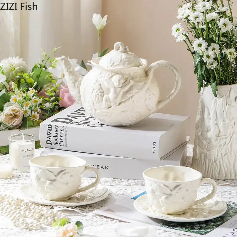 White ceramic angel relief ceramic teapot with intricate cherub and foliage detailing on stacked books from decorbites relief ceramic tableware set
