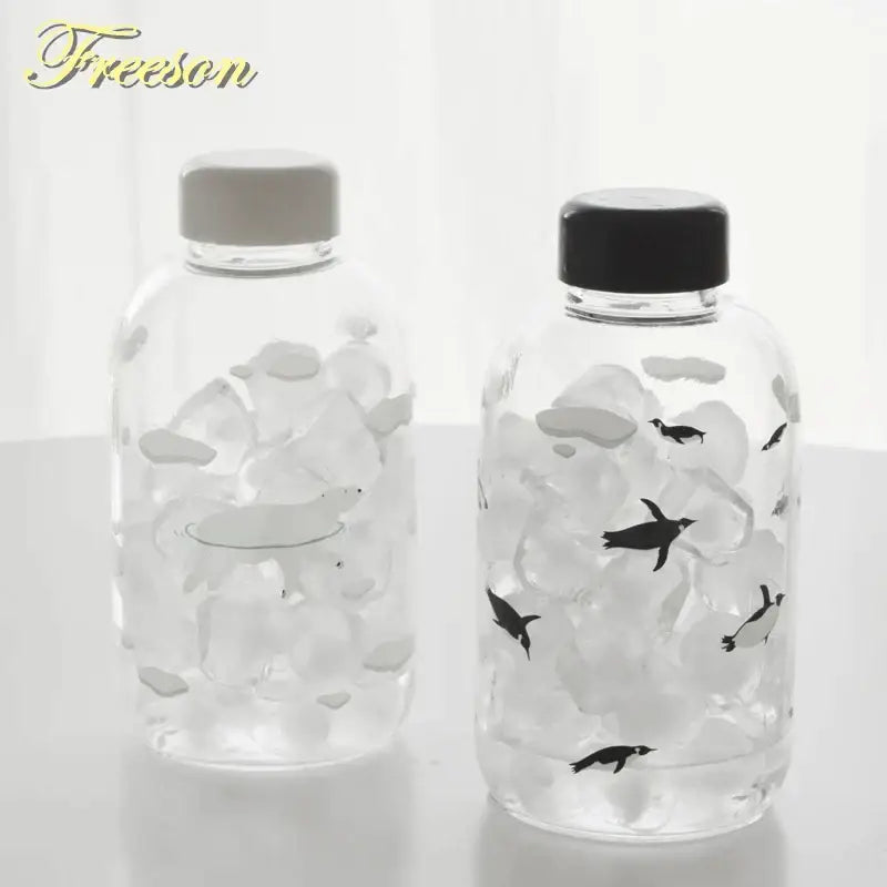DecorBites™ animal glass water bottle with clear body, penguin design, black and gray caps for outdoor use