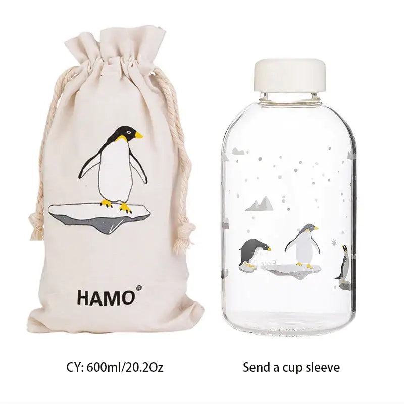 Clear glass water bottle with white cap and penguin illustration with matching beige drawstring sleeve for outdoor use
