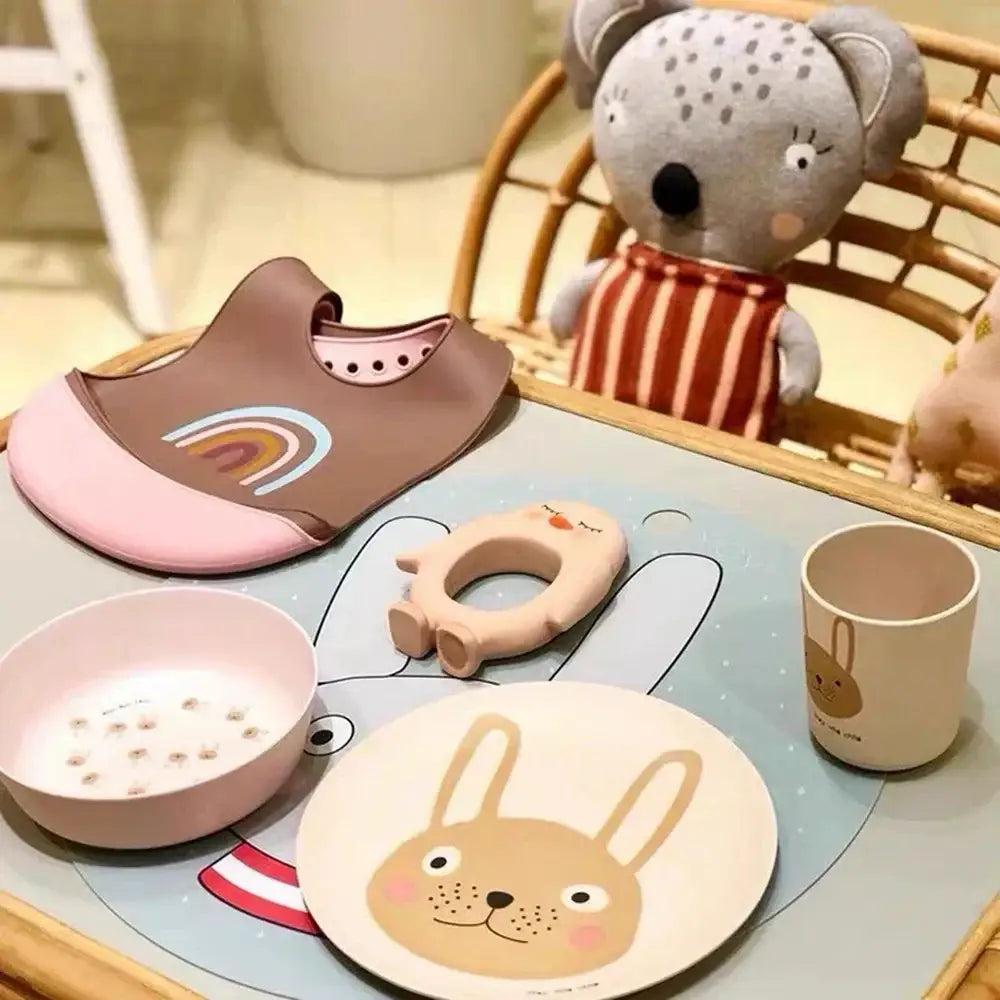 Pink and brown silicone baby bib with rainbow design paired with animal print bamboo fiber salad plate kitchen tableware