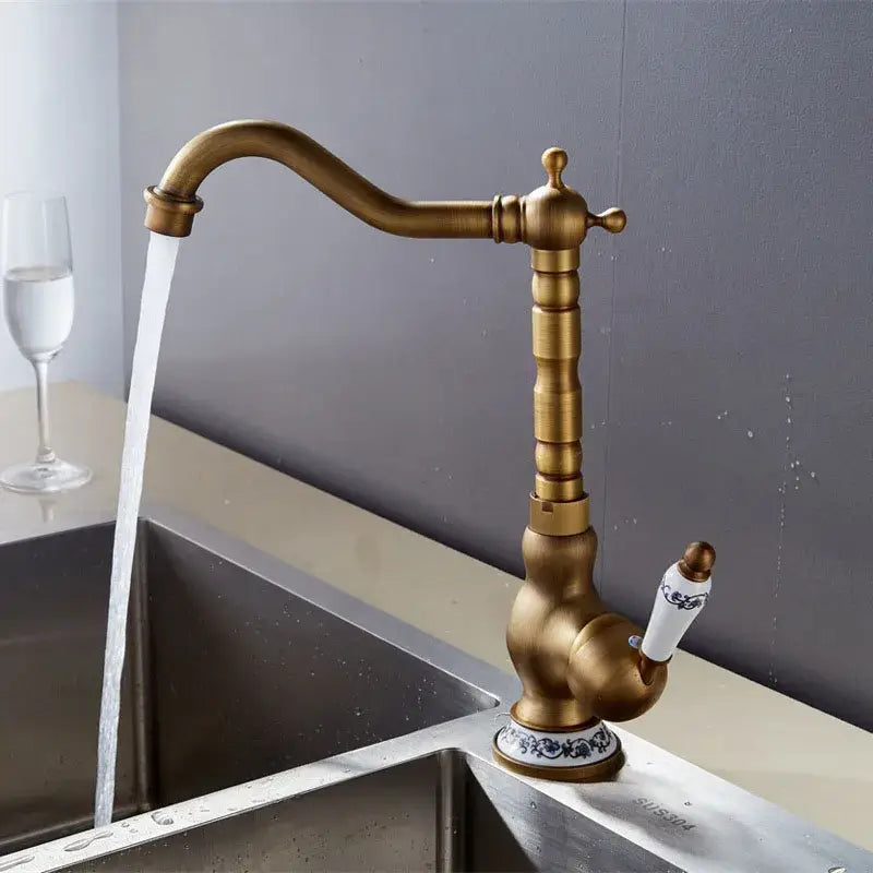 Decorbites antique brass basin faucet with ornate detailing and white ceramic handle featuring blue floral patterns