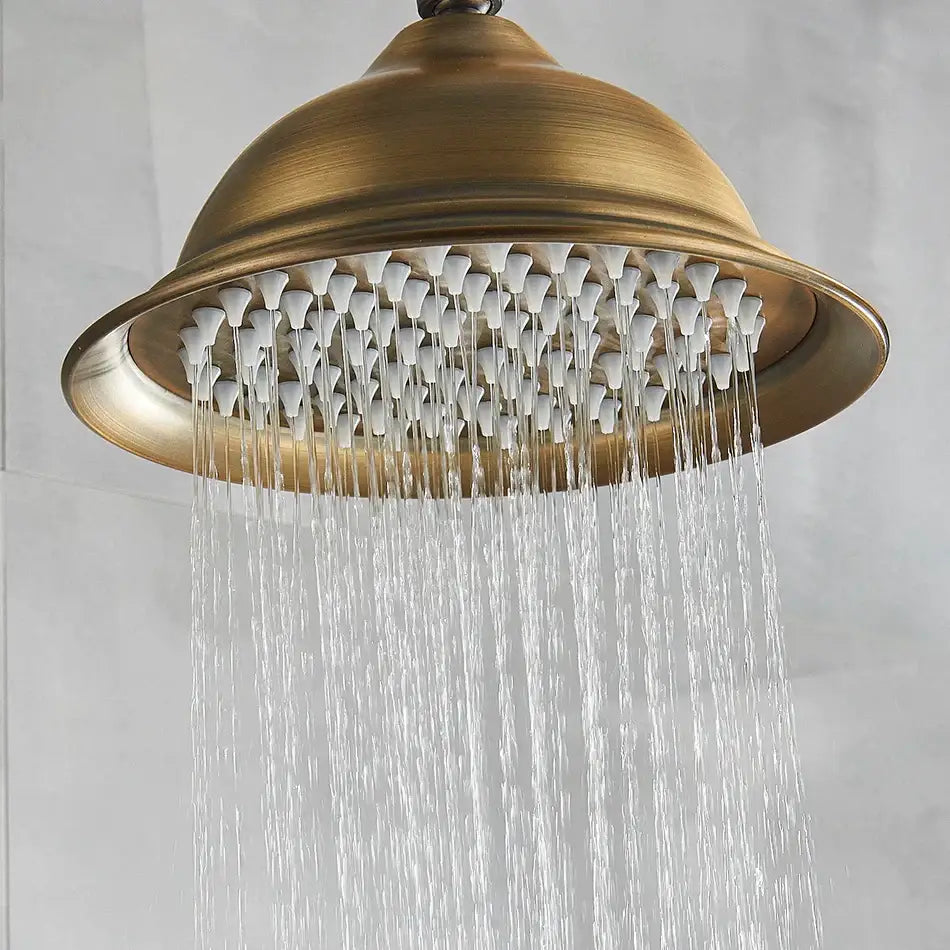 Antique brass bath rainfall shower head with multiple white nozzles spraying water in brass finish