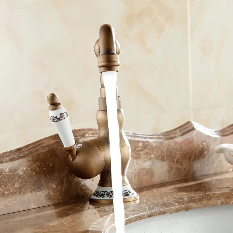 Antique brass bathroom sink faucet with white ceramic handle and black floral patterns by DecorBites™