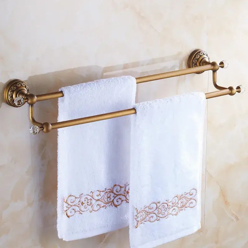 DecorBites antique brass double towel bar with crystal accents holding white towels with gold embroidered borders