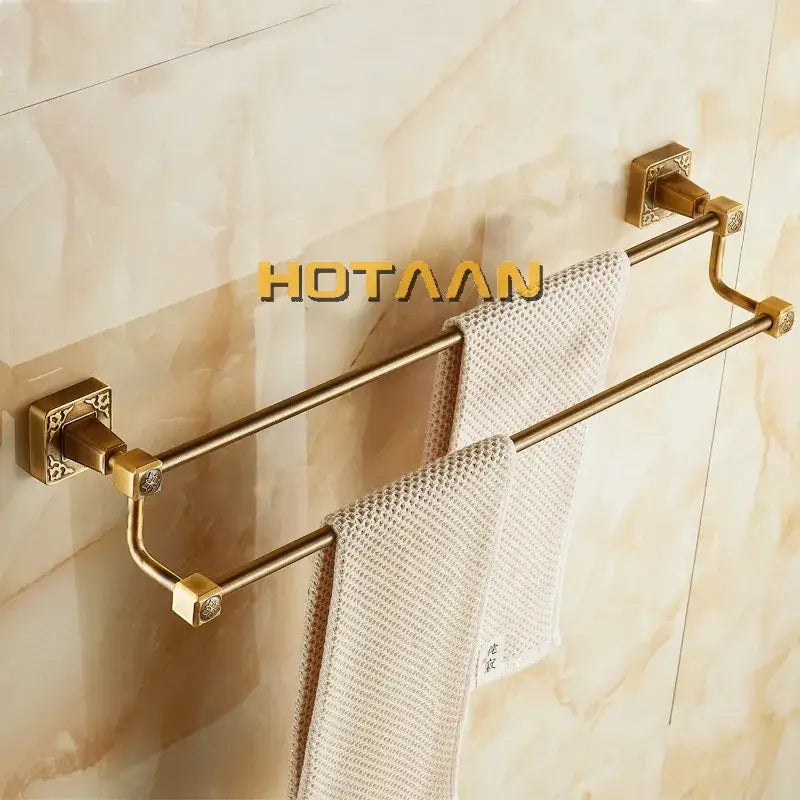 Gold-toned double towel bar with ornate square brackets and textured beige towels in antique brass finish aluminum