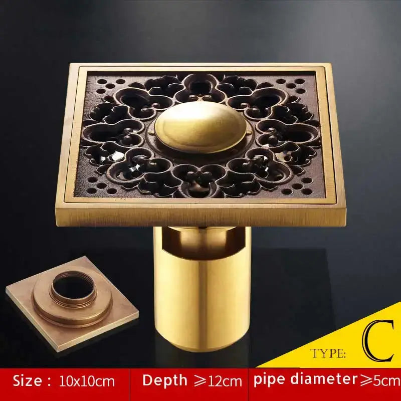 Brass square shower drain with ornate floral cutout and central dome finish in antique brass fish style by DecorBites