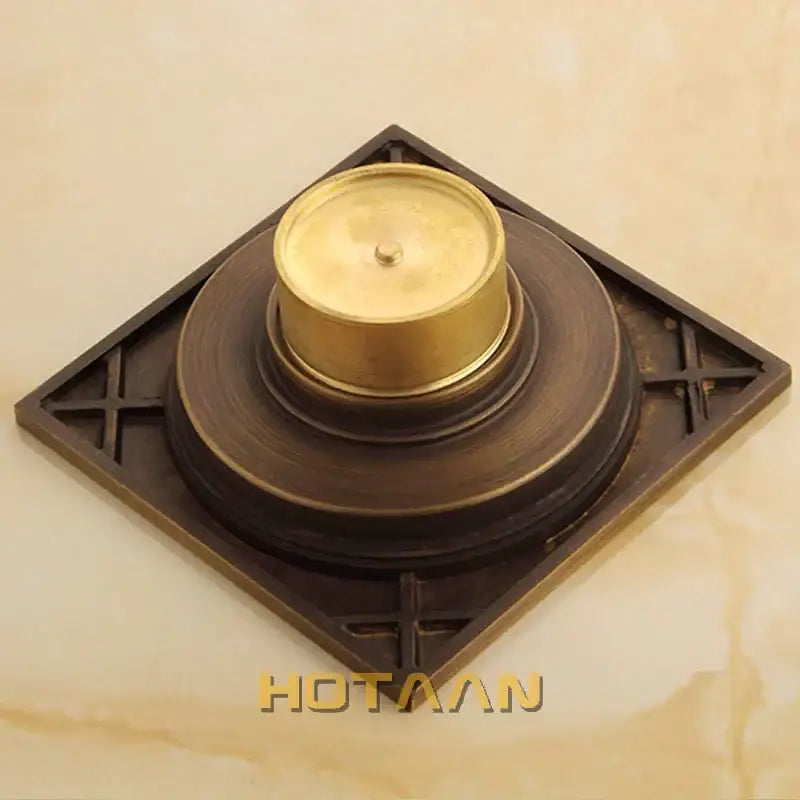 Brass-colored antique brass flower art floor drain with decorative cross patterns and golden-toned central component