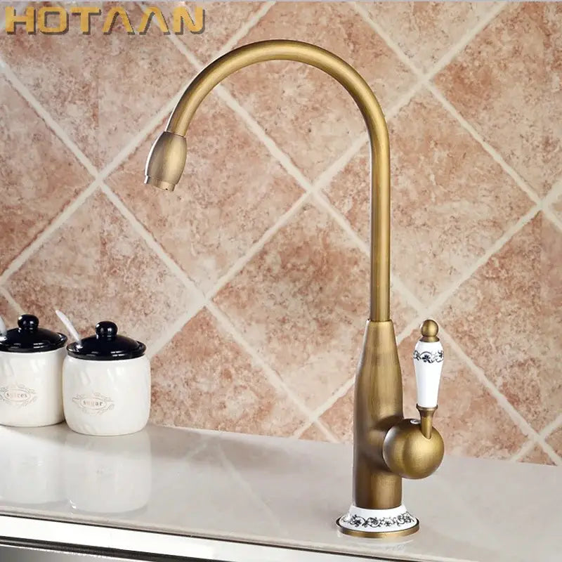 Antique brass kitchen faucet decorbites with curved spout and ornate white ceramic handle with black floral detailing